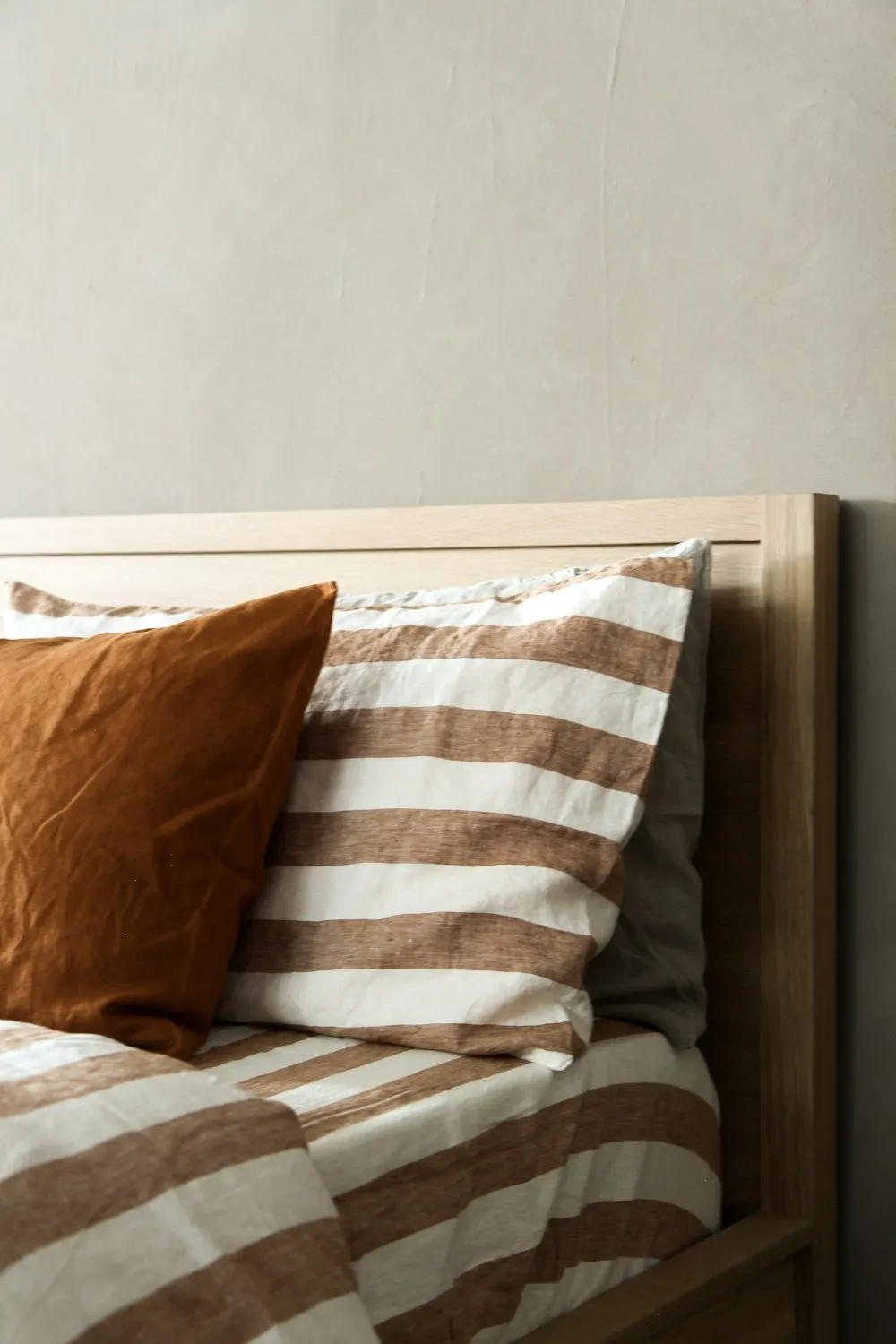 Close-up of a rust and cream striped cushion against warm bedding, showing a coordinated material palette.